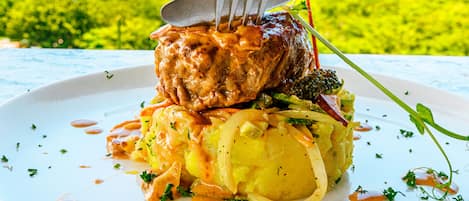 A plate of food with a fork and knife, a scenic view of a body of water and greenery in the background.