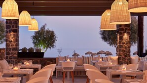 An outdoor dining area with stone pillars, wicker lamps, and tables set for two with candles. - Aqua Blue Hotel (Santorini)