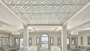 A spacious, modern living area with a large glass door leading to a balcony with a view of the beach. - Aqua Blue Hotel (Santorini)
