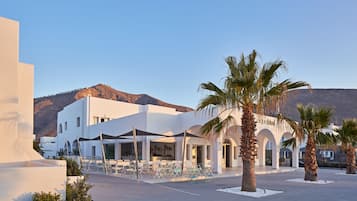 Un edificio blanco con un patio, palmeras y una montaña al fondo.