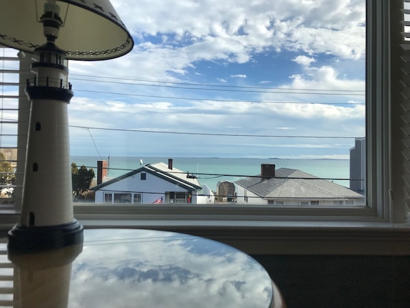 Une vue depuis une fenêtre, avec une lampe au premier plan, un ciel dégagé et des bâtiments visibles de l’autre côté de l’eau.