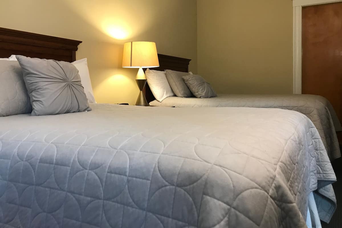 Two beds with grey quilts, a bedside lamp, and a wooden headboard.