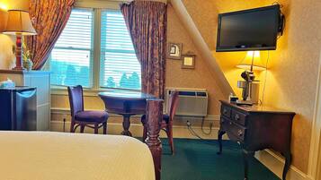 A hotel room with a bed, a desk, a chair, a television, and a window with curtains.