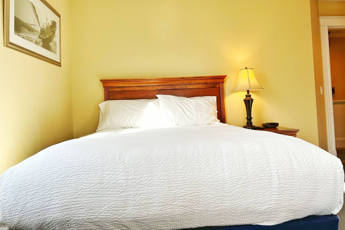 A neatly made bed with white linens in a room with yellow walls.