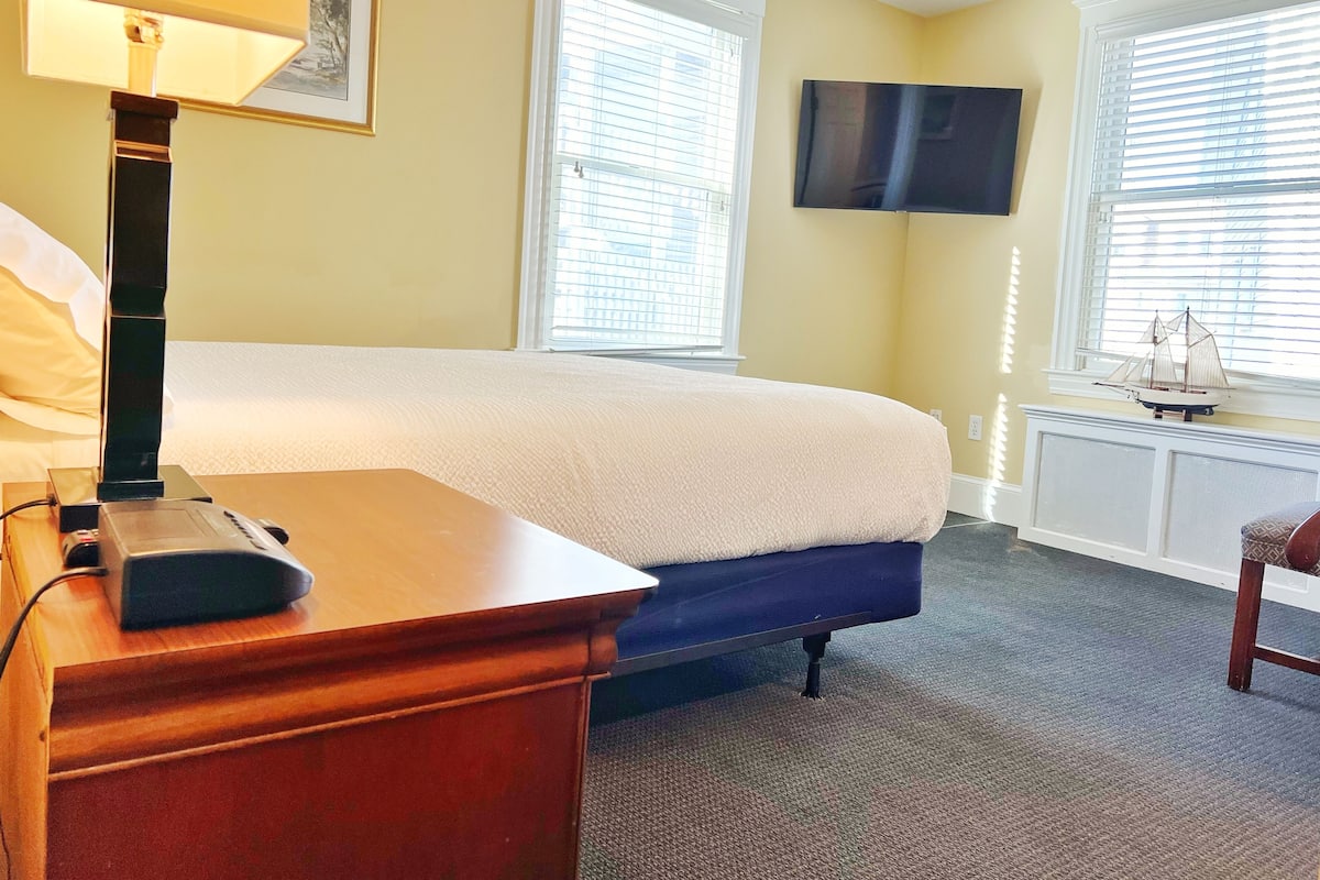 A hotel room with a bed, a desk, a lamp, a television, and a window with blinds.