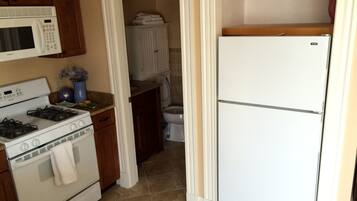 Una cocina con estufa, microondas y refrigerador. Hay un armario de madera sobre la estufa y un pequeño estante encima del refrigerador.