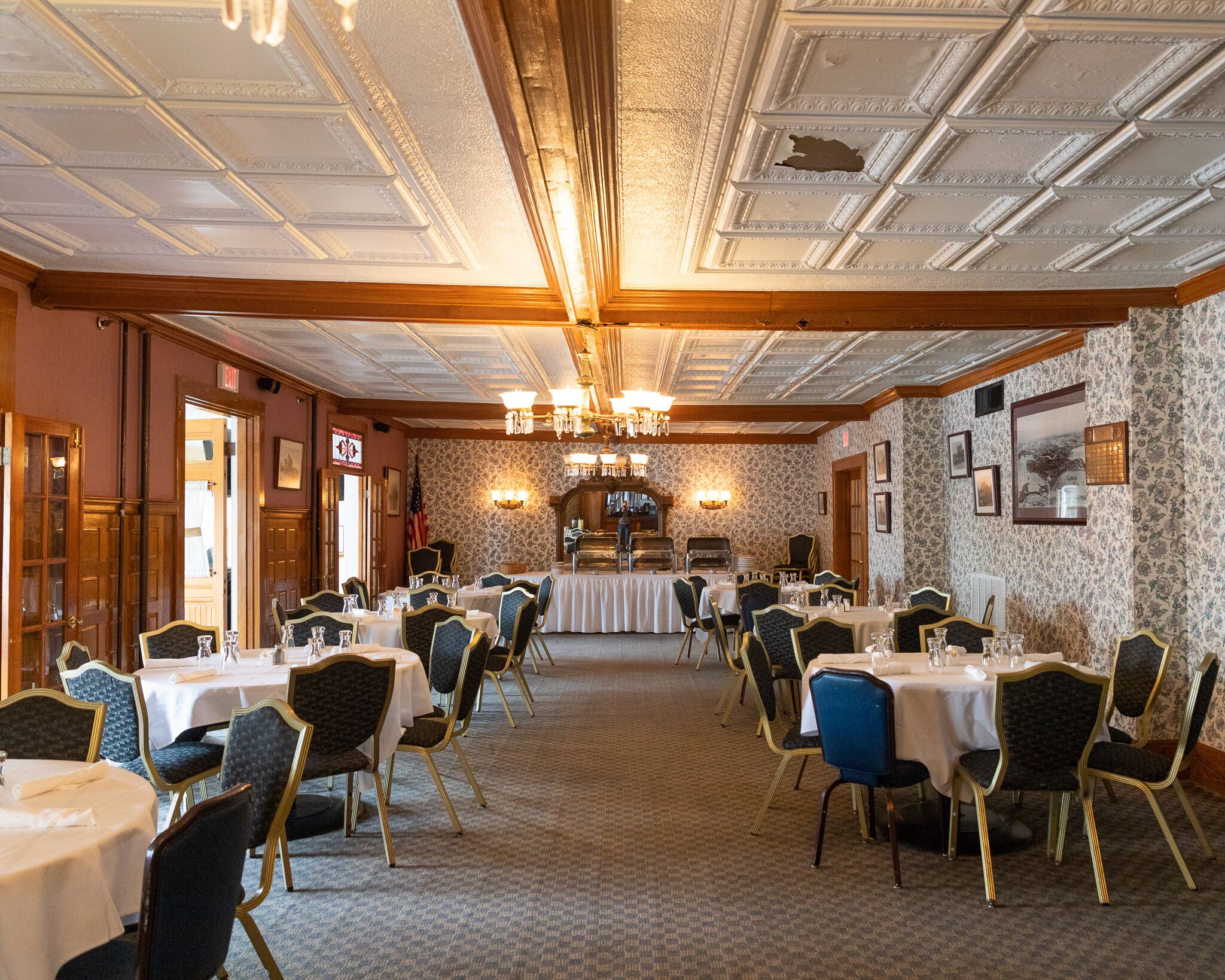 A banquet hall with multiple round tables, chairs, and a central buffet area.
