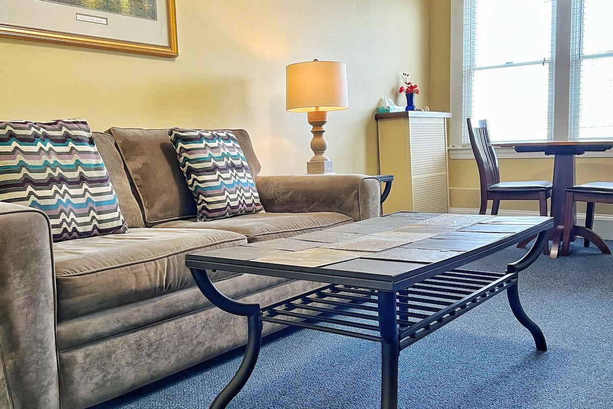 A living room with a sofa, a coffee table, a lamp, and a dining table with chairs.