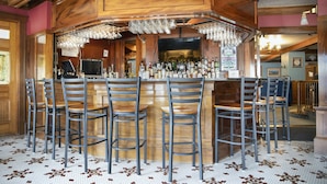 A bar area with a wooden counter, multiple bar stools, and a variety of bottles and glasses. - The Winthrop Arms Hotel And Restaurant (Winthrop)
