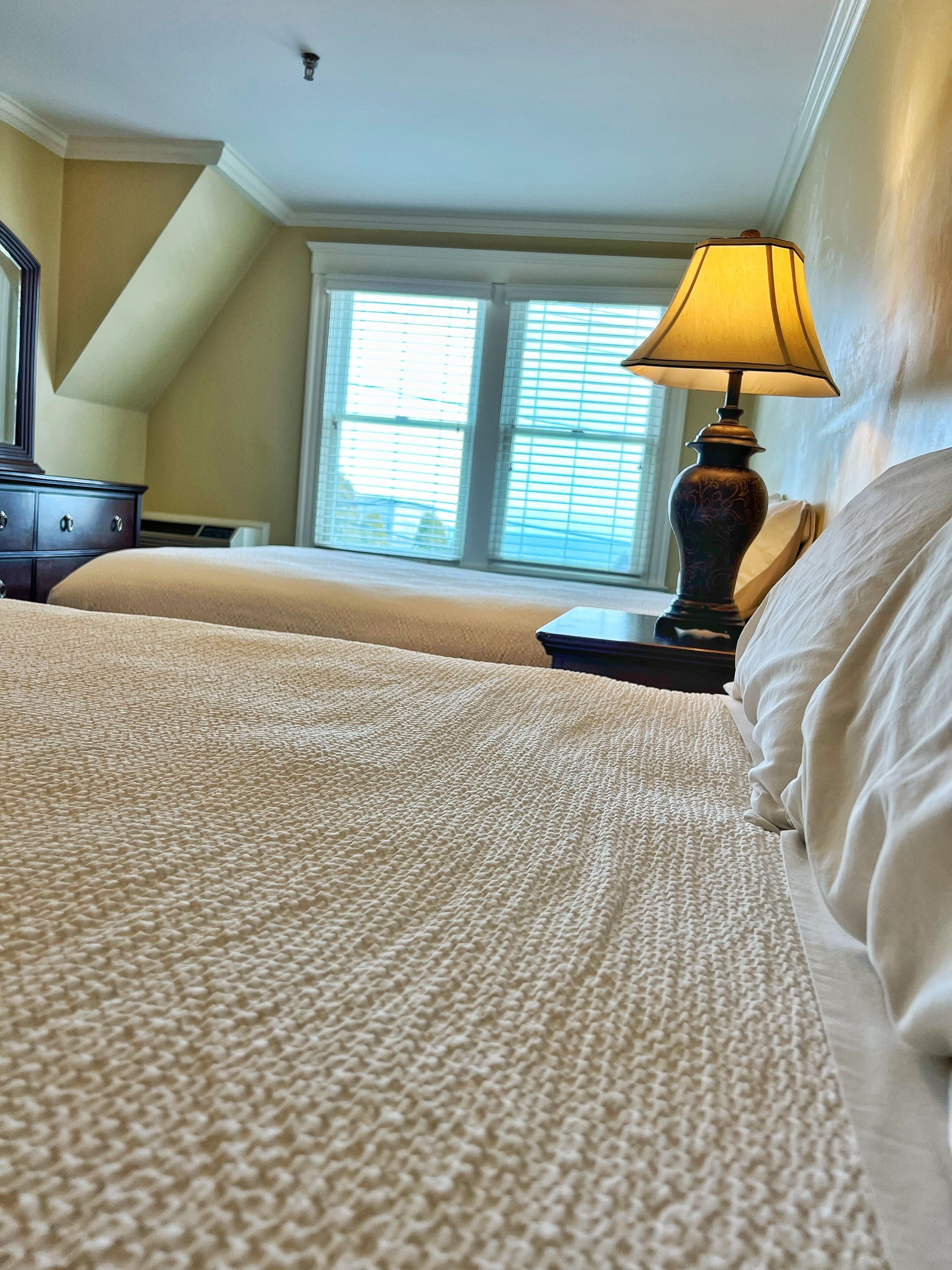 Quarto com uma cama grande, mesa de cabeceira, luminária e janela com persianas.