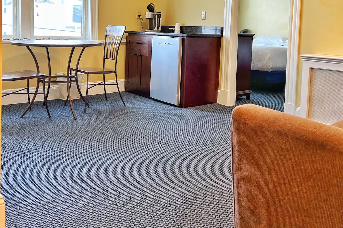 A compact hotel room with a kitchenette, a dining area with a table and chairs, a single bed, and a TV mounted on the wall.