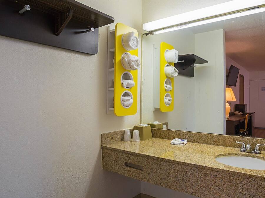 Een badkamer met een granieten aanrecht, een wastafel, een spiegel en een handdoekrek met meerdere handdoeken.