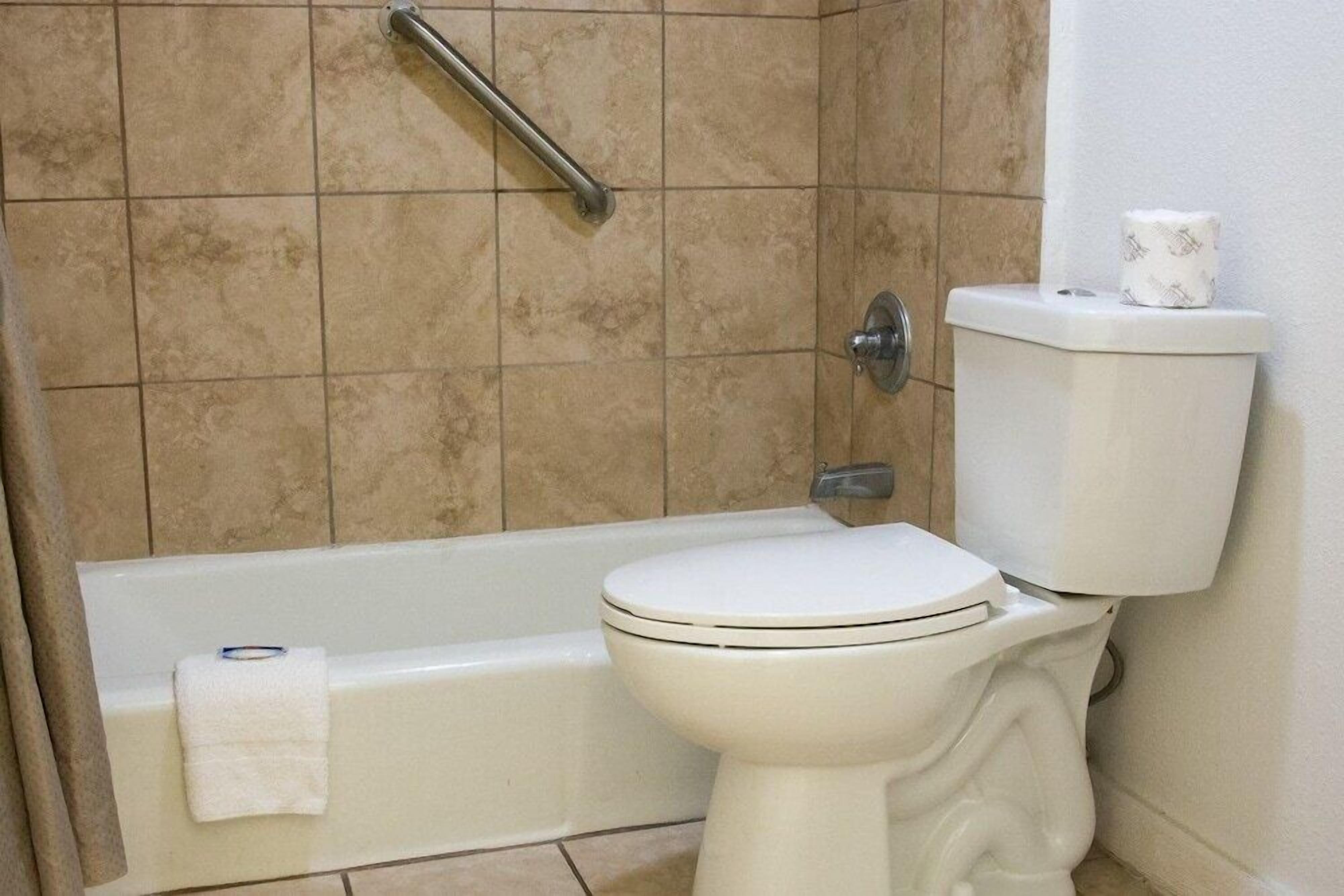 A bathroom with a bathtub, toilet, and a handrail.