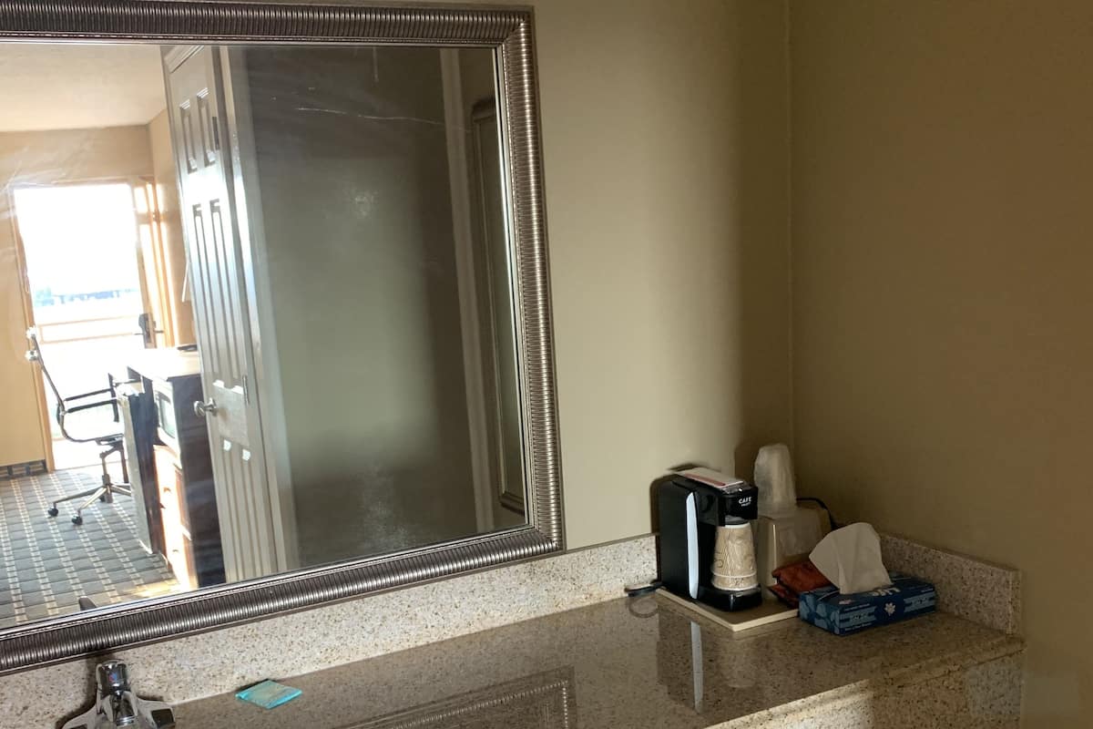 A bathroom with a granite countertop, a sink, a mirror, and a towel dispenser.