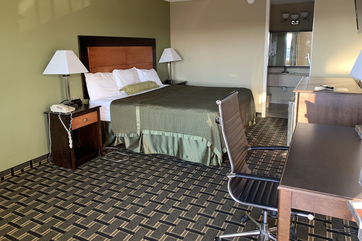 A hotel room with a bed, bedside tables, a desk, and a kitchenette.