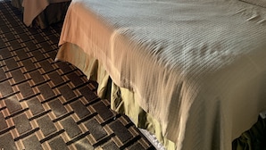 Habitación de hotel con dos camas, alfombra estampada y una ventana con cortinas.