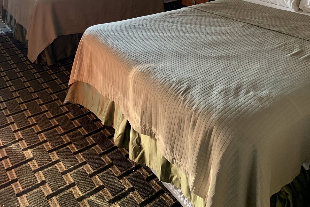 A hotel room with two beds, a patterned carpet, and a window with curtains.