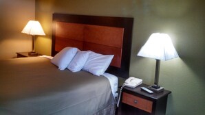 A hotel room with a bed, two bedside lamps, a nightstand with a phone, and a drawer.