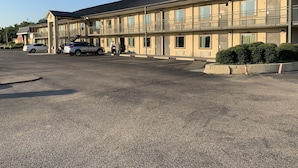 Un motel con estacionamiento, un área exterior techada y un edificio con múltiples ventanas y balcones.