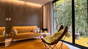 Una sala de estar moderna con un sofá, un sillón y un amplio ventanal con vistas a árboles.
