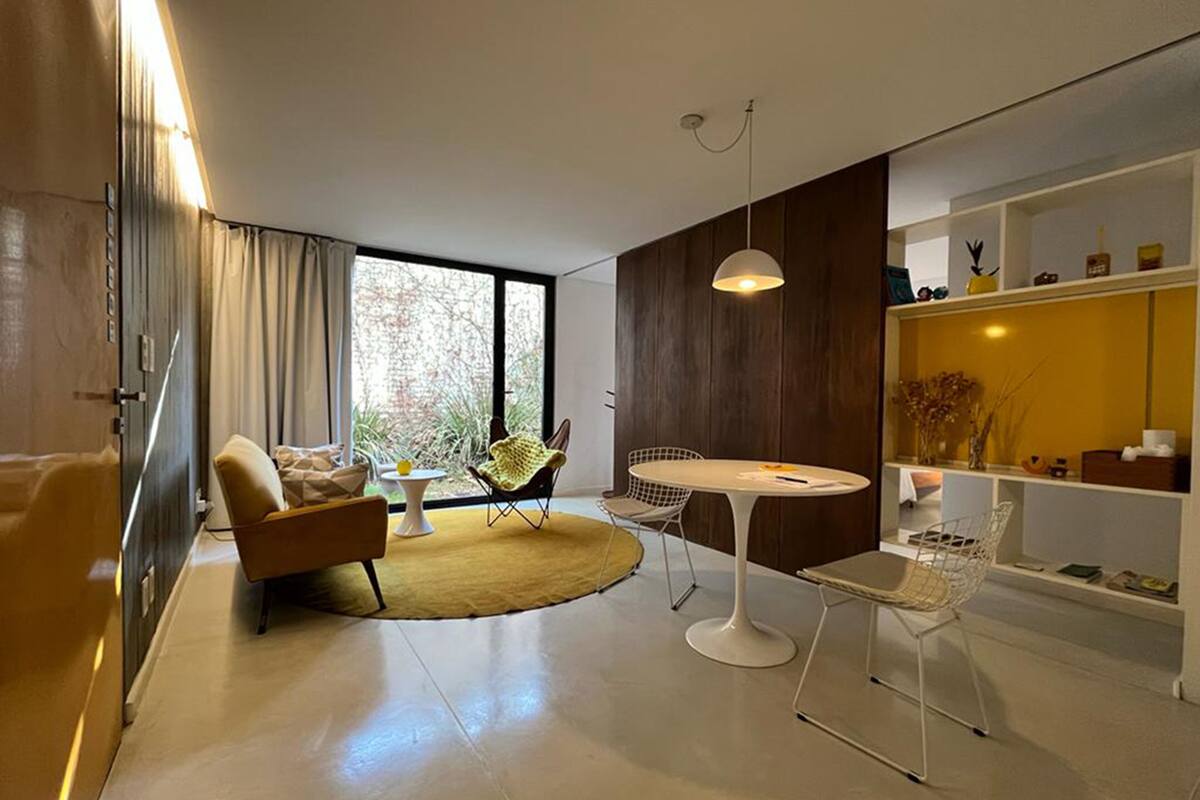 A modern living room with a sofa, a round table, and chairs. There is a large window providing natural light.