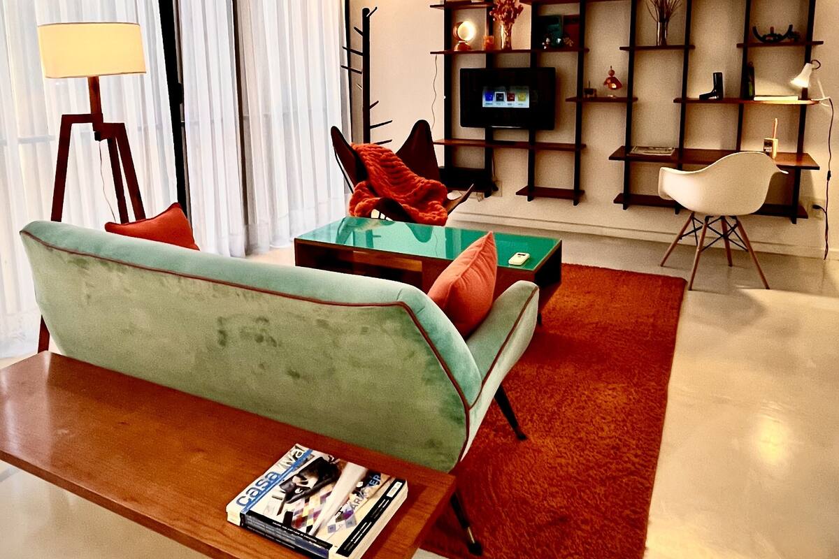 A modern living room with a green sofa, a wooden coffee table, and a TV on a wooden shelf.