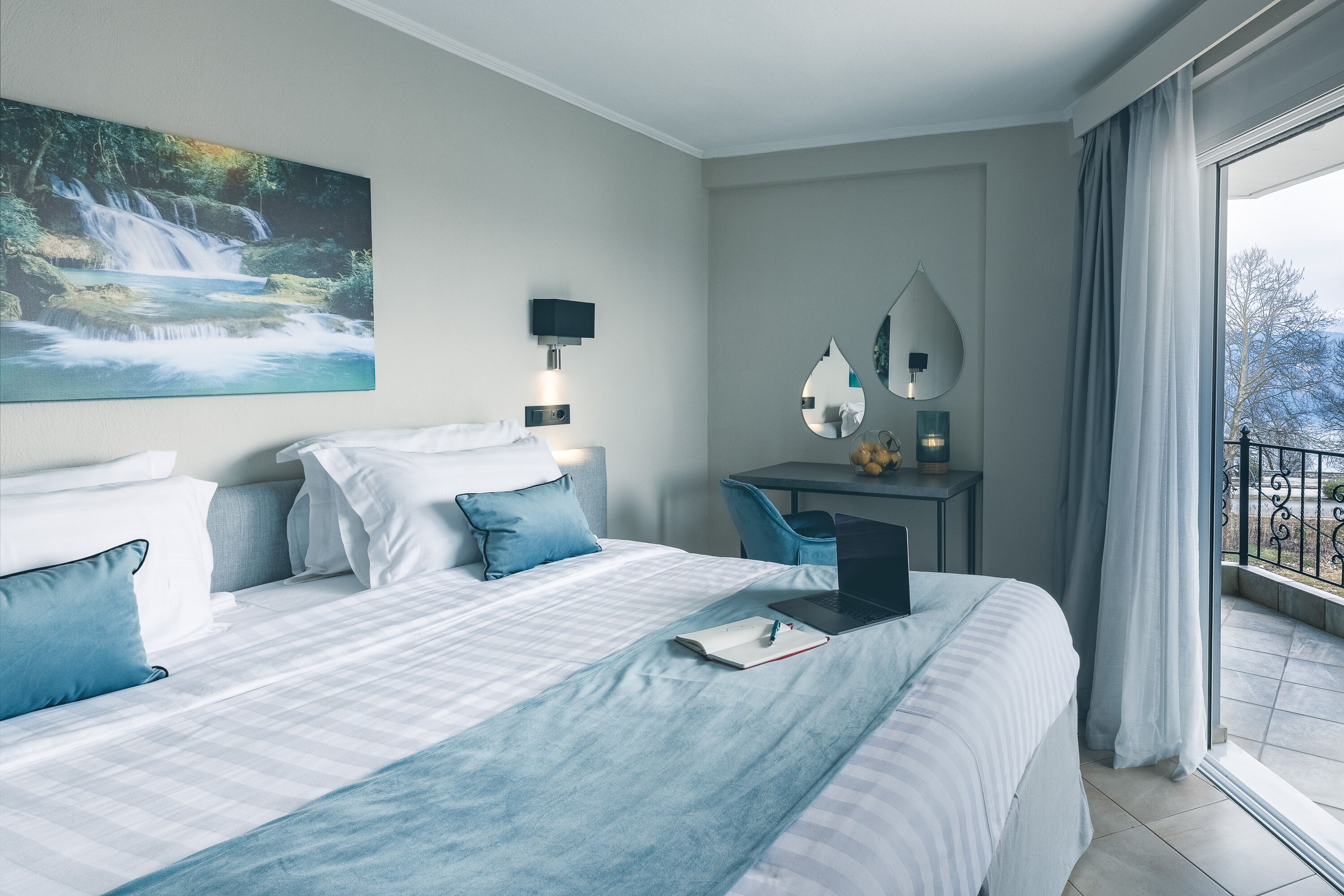Habitación de hotel con una cama grande, un escritorio con una computadora portátil, un espejo y vistas a un balcón.