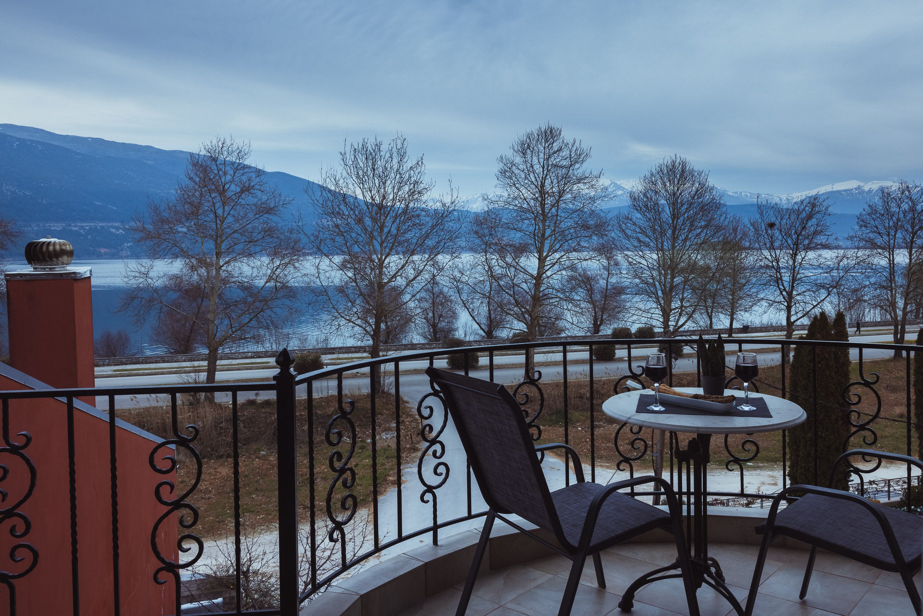 A balcony with a table and chairs, overlooking a snowy landscape and a body of water.
