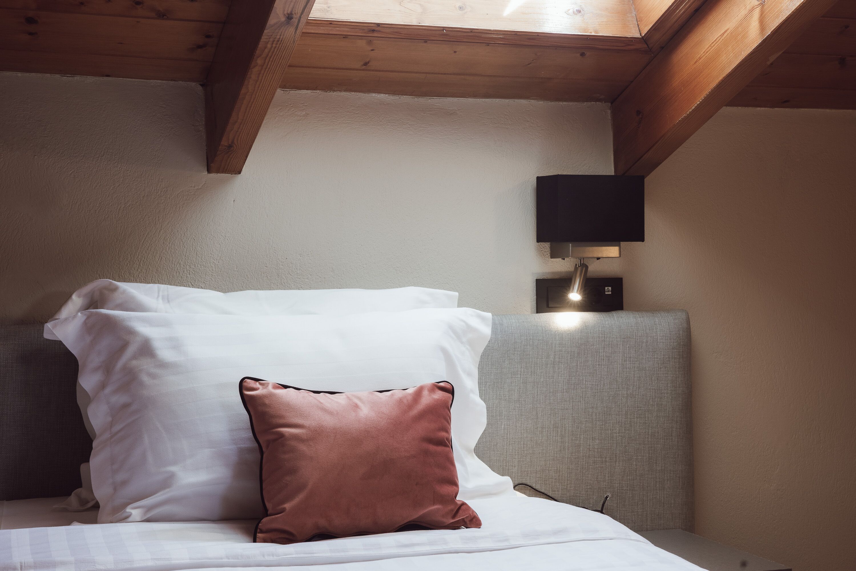 A bed with white and brown pillows, a grey headboard, and a wall-mounted light fixture.
