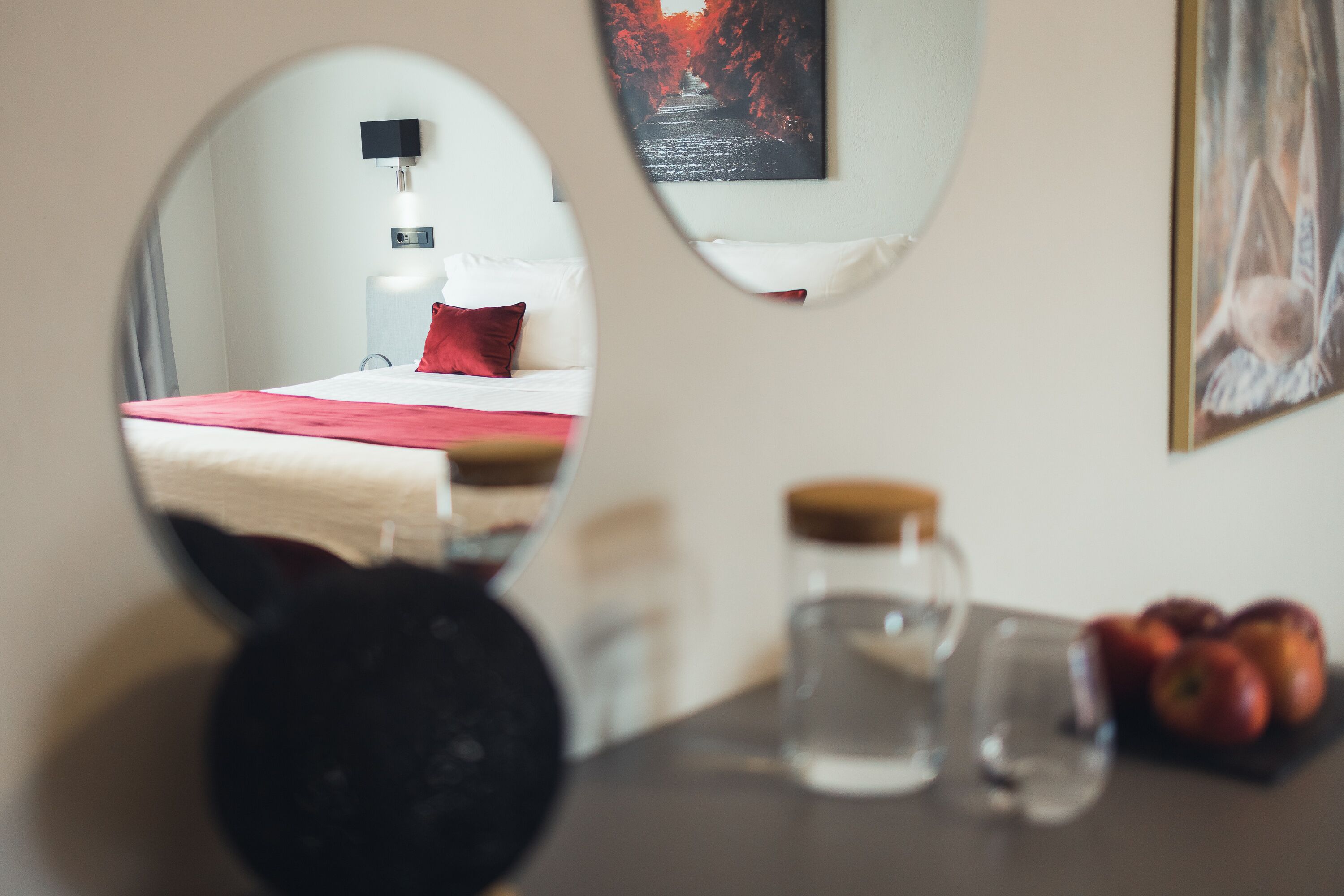 Un dormitorio con cama, mesita de noche con lámpara, espejo y un cuadro en la pared.