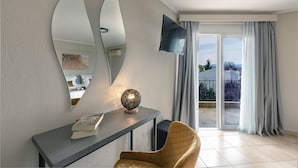 Een moderne woonkamer met een grote spiegel, een flatscreen televisie, een ronde tafel met een boek en uitzicht op de buiten omgeving via een schuifdeur.