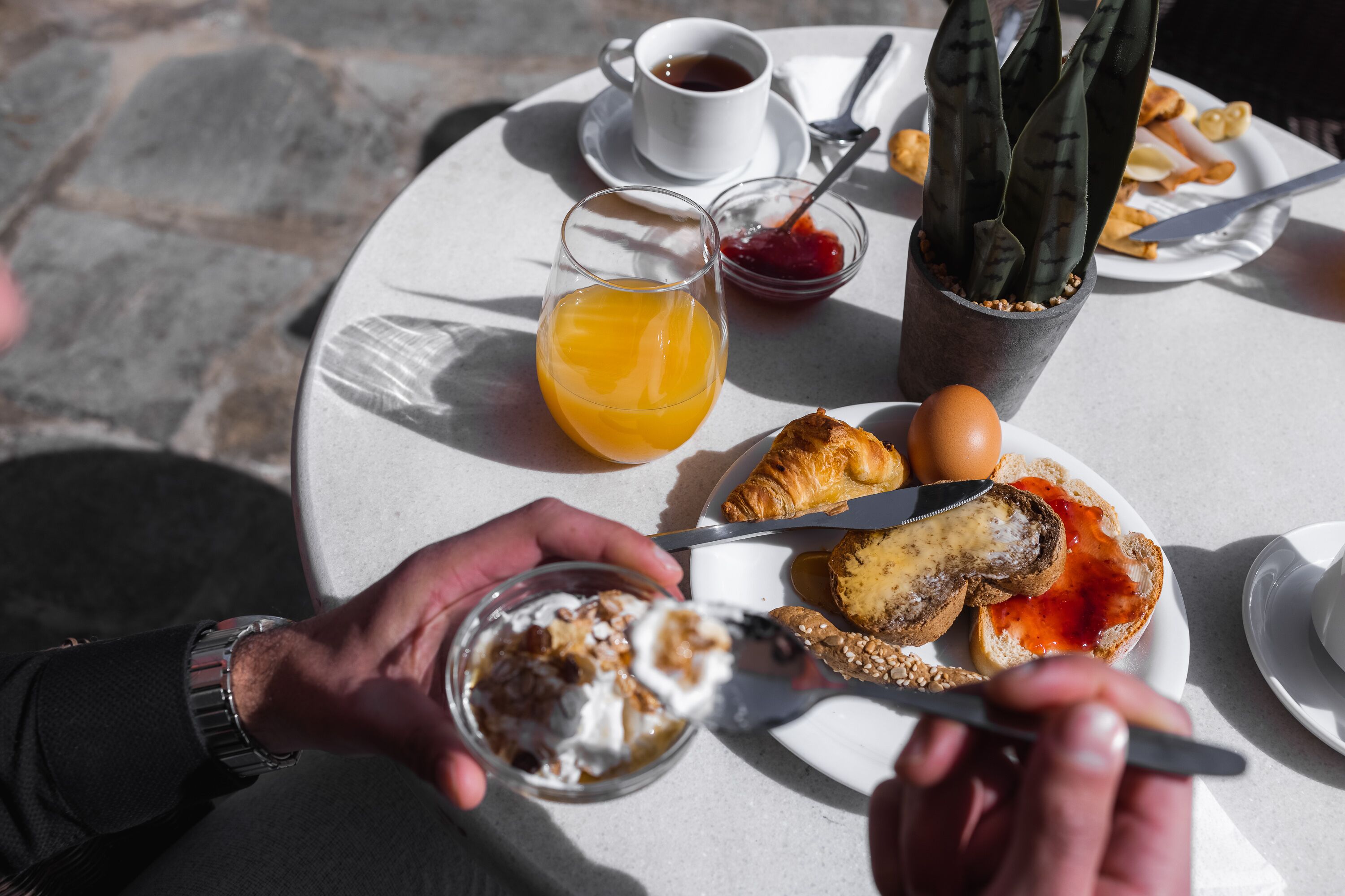 Un desayuno con un croissant, un vaso de jugo de naranja, una taza de café y una pequeña planta en maceta sobre una mesa redonda.