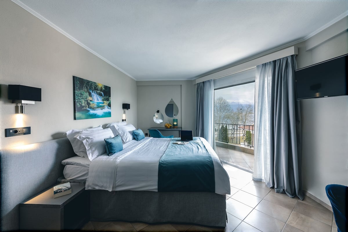 Ein modernes Hotelzimmer mit einem großen Bett, einem Schreibtisch, einem Laptop und Blick ins Freie.