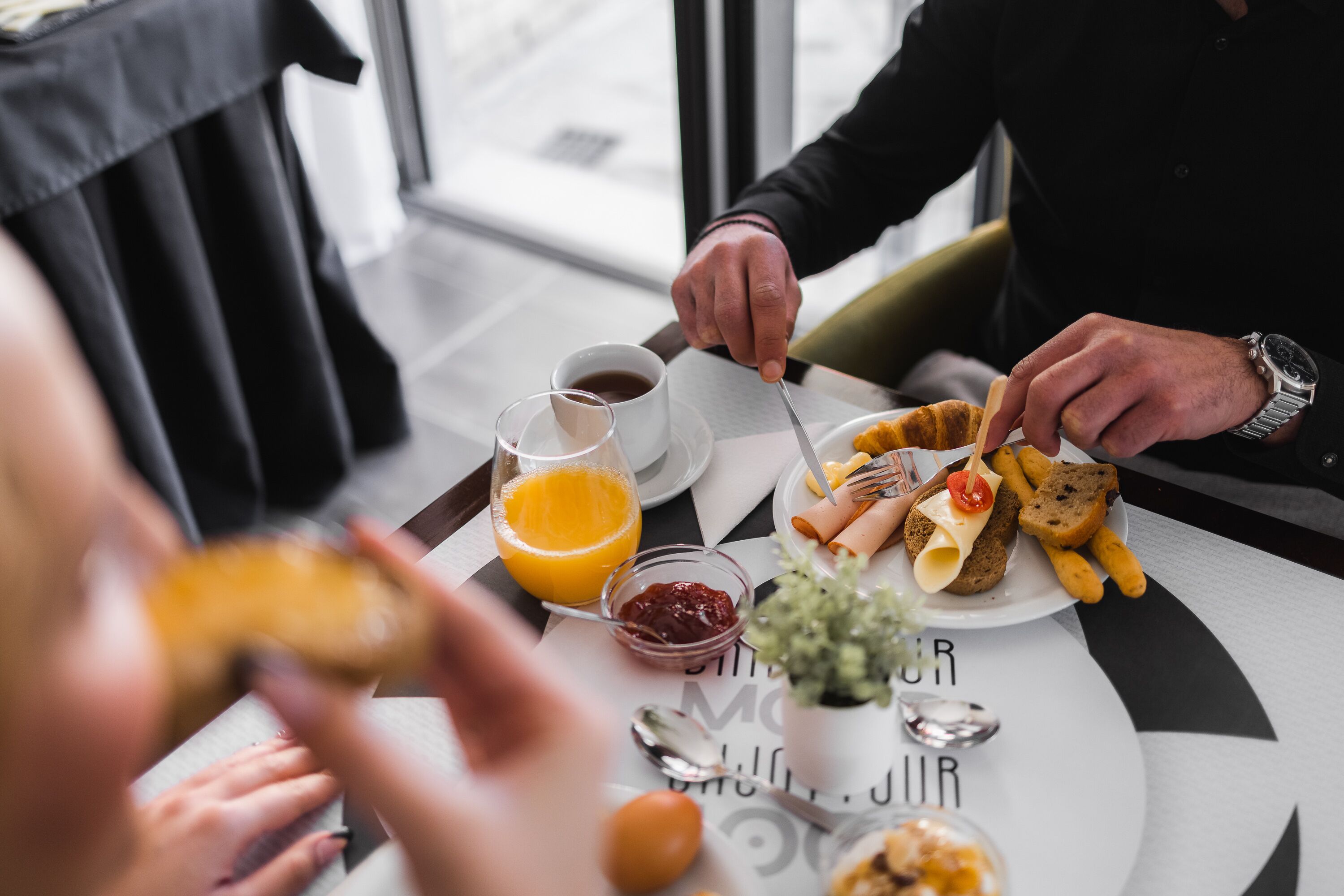 A dining table with a meal consisting of bread, cheese, and a tomato. There are two cups, one with a beverage and the other empty.