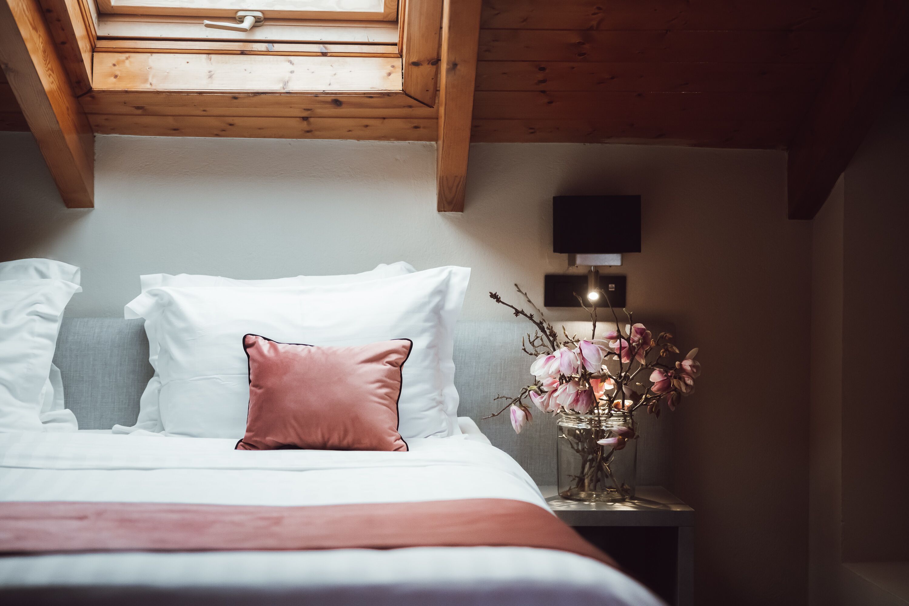 Ein Schlafzimmer mit Bett, Kissen, einem Nachttisch mit Blumenvase und einem an der Wand befestigten Fernseher.