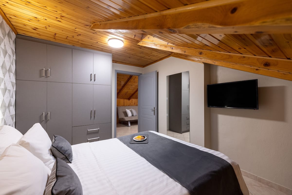 A bedroom with a bed, grey wardrobe, a flat-screen TV, and a wooden ceiling.