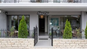 Un edificio con un cartel que dice "Navit" en la entrada, un camino de entrada con rejas y un pequeño espacio al aire libre con mesas y sillas.
