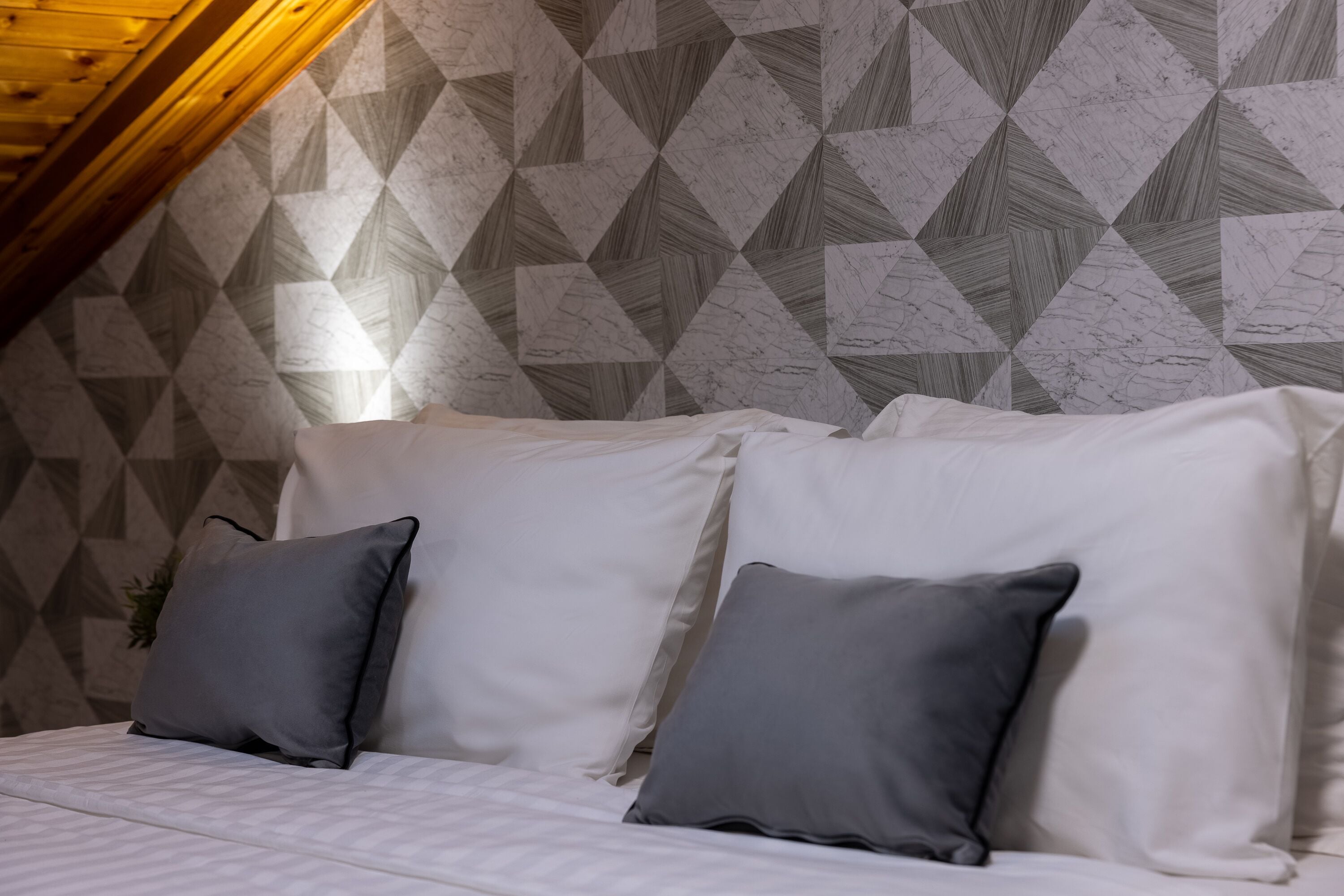 Un dormitorio con techo inclinado, una cama con ropa de cama blanca y almohadas grises.