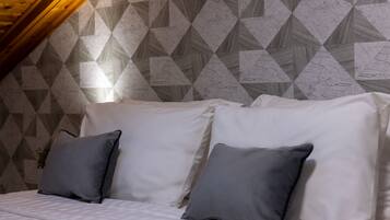 Un dormitorio con techo inclinado, una cama con ropa de cama blanca y almohadas grises.