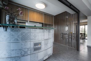 Un espace d’accueil doté d’un comptoir en marbre, d’un vase en verre contenant des fleurs et d’un mur recouvert de panneaux en bois.