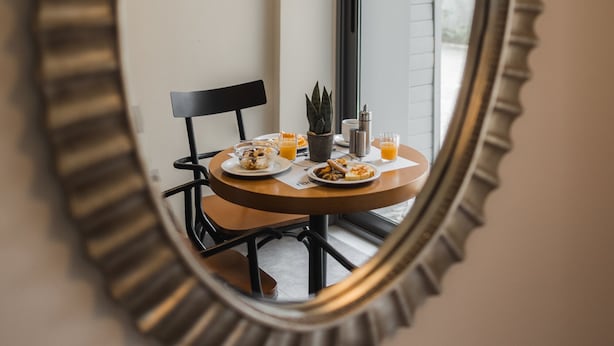 Una mesa redonda con una silla, una pequeña planta en maceta y un vaso de jugo de naranja.