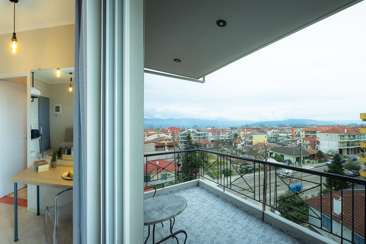 A balcony with a view of a residential area, a bedroom with a bed and a desk, and a bathroom with a mirror and a towel rack.