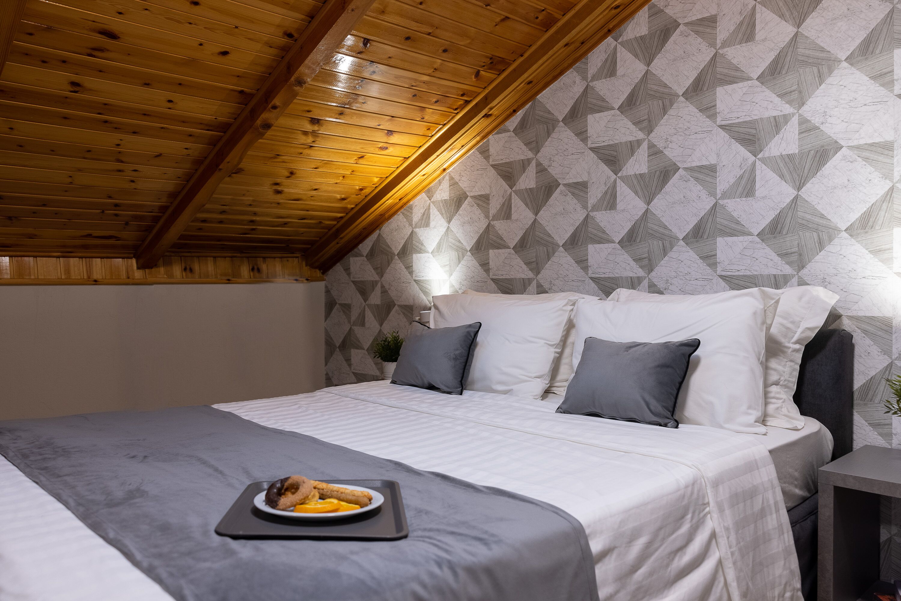 Ein Schlafzimmer mit Holzbalkendecke, einem Bett mit weißer und grauer Bettwäsche sowie einer Teller mit Essen auf dem Bett.