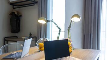 Una computadora portátil sobre una mesa de madera con dos lámparas, un cuenco de limones y un perchero en una habitación con ventana y cortinas.