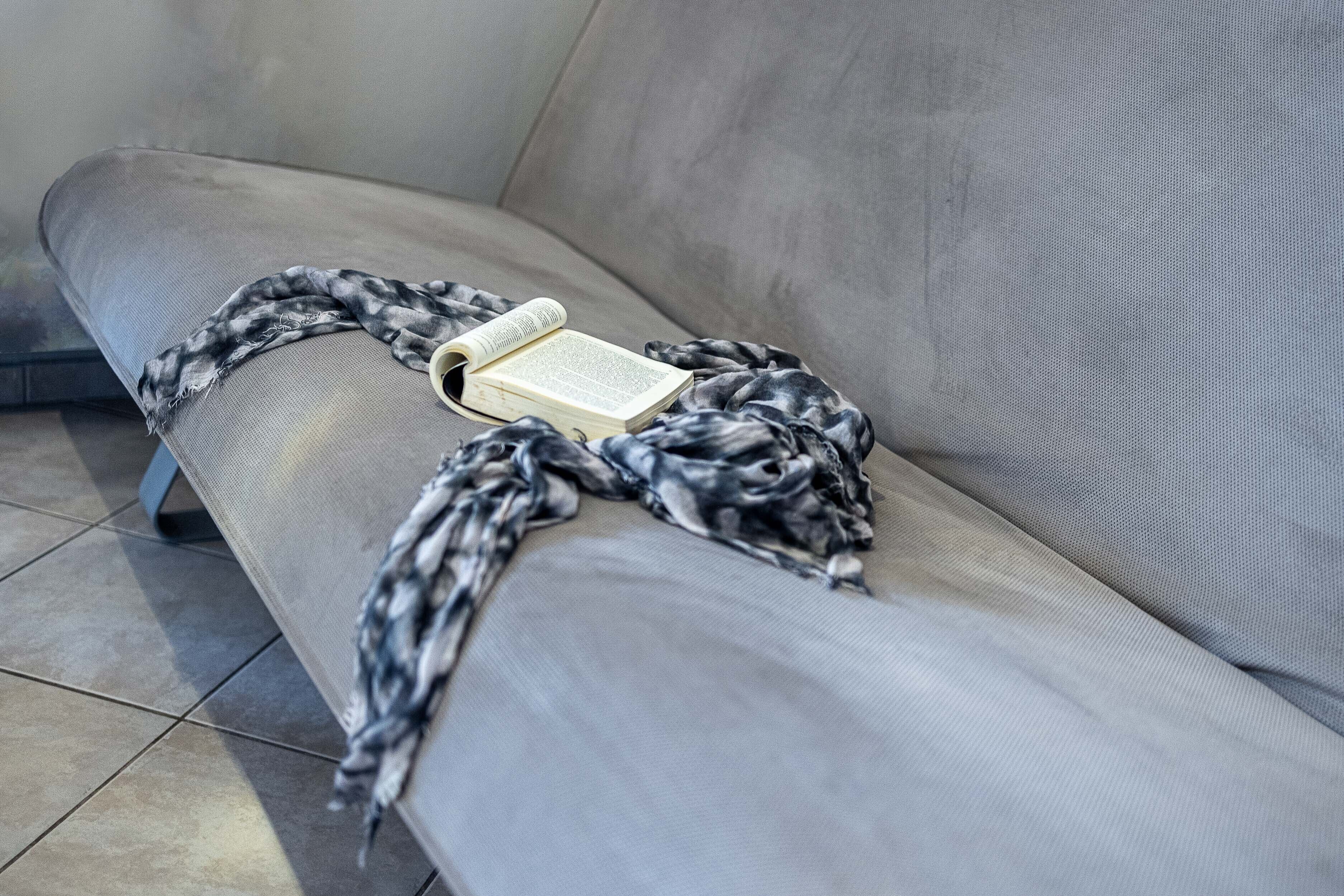 A grey sofa with a book and a black and white patterned blanket.