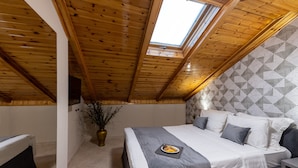 Un dormitorio con techo inclinado, tragaluz, cama con cubrecama gris y un plato decorativo sobre la cama.