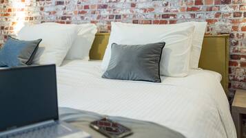 A bed with white linens and two pillows, a laptop on the bed, and a smartphone on the bedside table.
