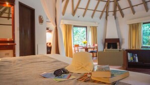 Une chambre d’hôtel avec un lit, une table sur laquelle se trouvent un chapeau et des livres, une cheminée et une vue sur l’extérieur.