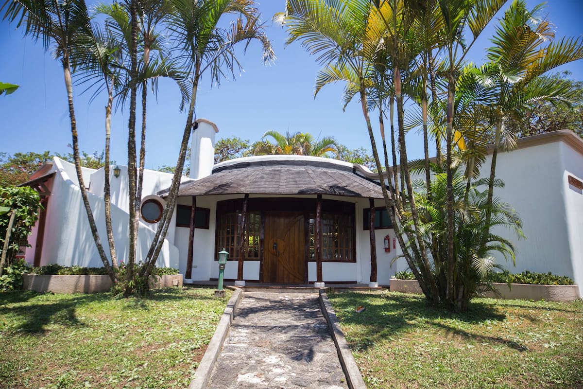 A white building with a curved roof, surrounded by palm trees and a paved pathway leading to a wooden door.