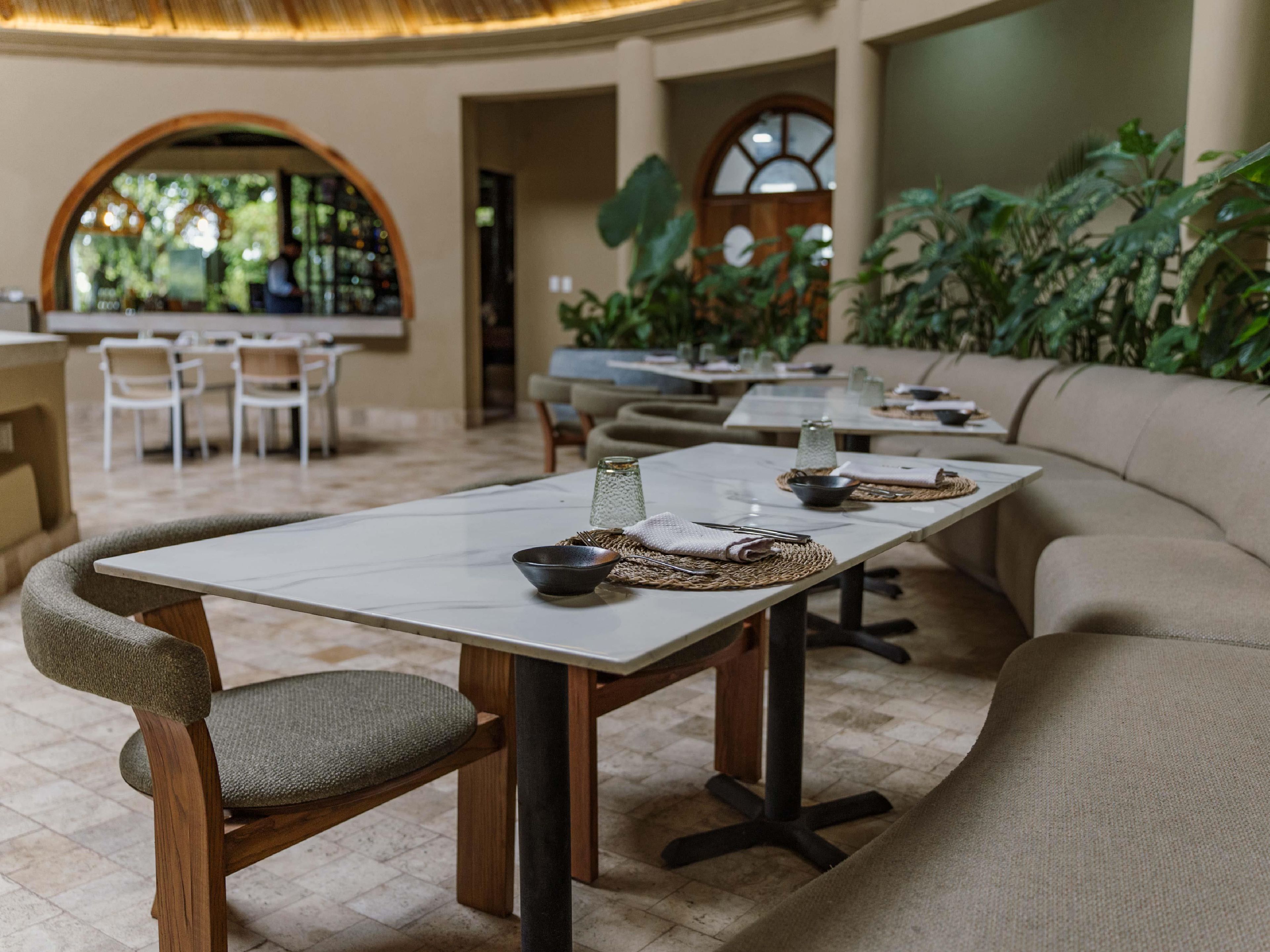 Un restaurante con una larga mesa común, sillas acolchadas y una zona de bar al fondo.